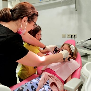 Odontóloga realiza fotografía intraoral a una niña con retractores mientras otra niña observa en Presencia Dental