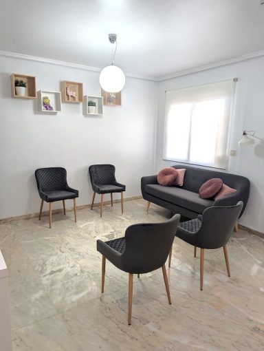 Sala de espera de Presencia Dental en Puçol con sofá y sillas grises, luz natural y decoración minimalista