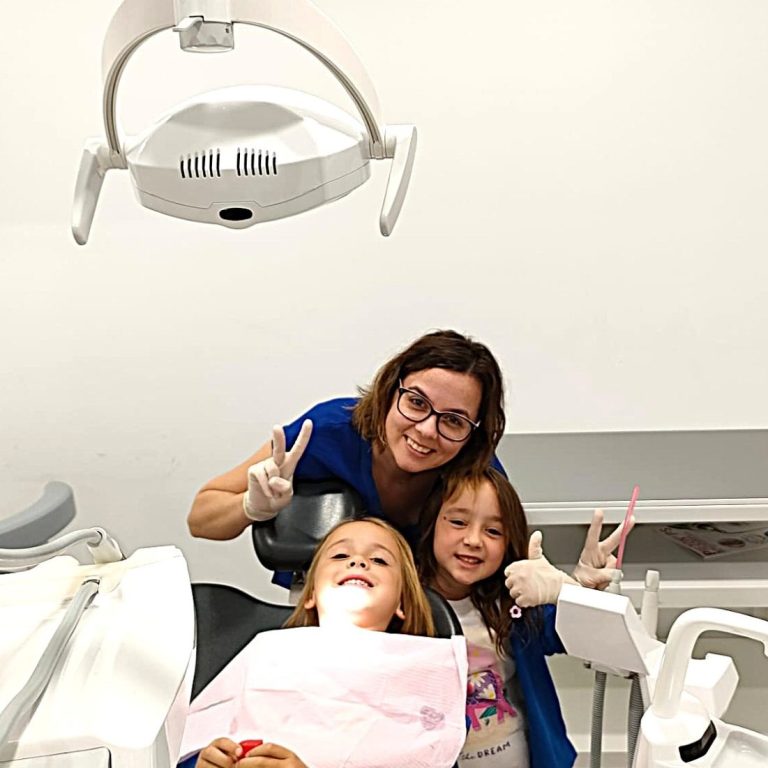 Dentista y dos niñas sonríen en el gabinete; visita infantil tranquila en Presencia Dental