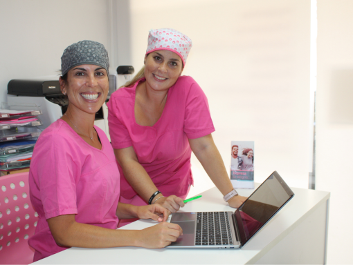 Dos profesionales de Presencia Dental, con bata rosa, explican un plan de tratamiento en un portátil y sonríen a cámara