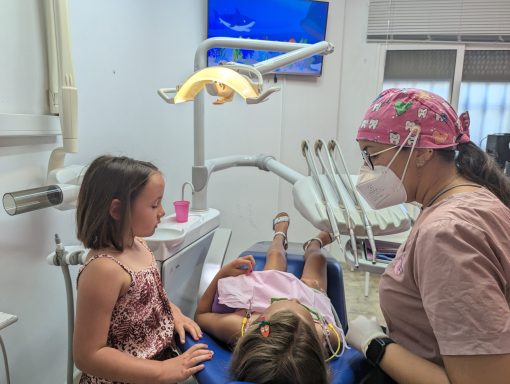Higienista atiende a una niña mientras su hermana observa; consulta infantil con dibujos animados en Presencia Dental